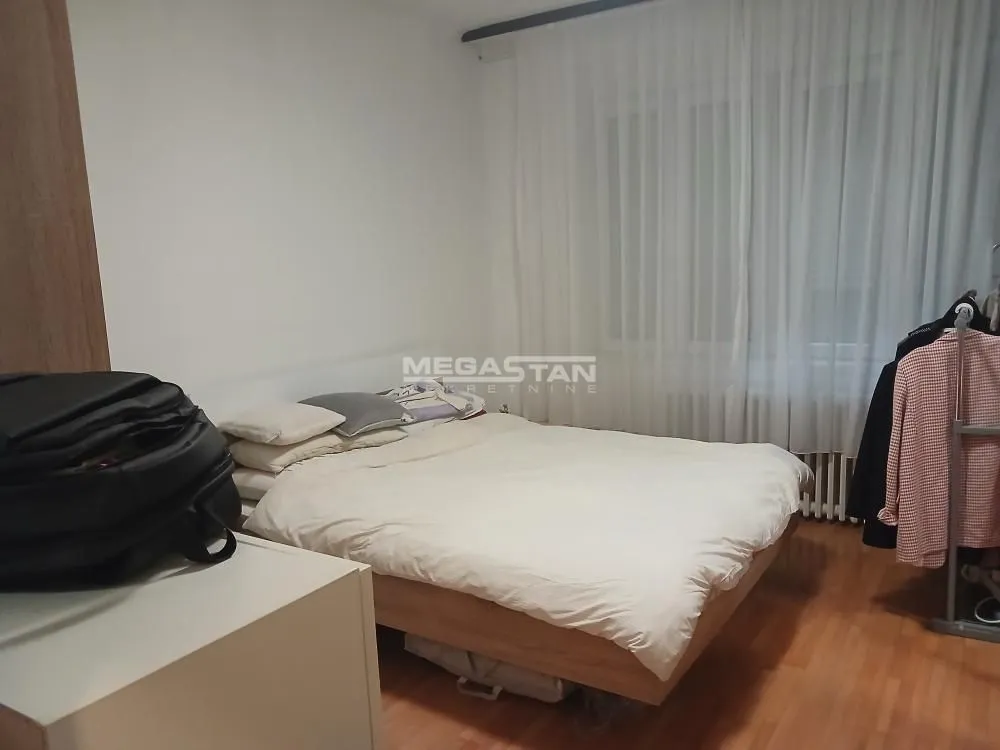 Nameštena spavaća soba sa bračnim krevetom i prozorom prekrivenim zavesama.