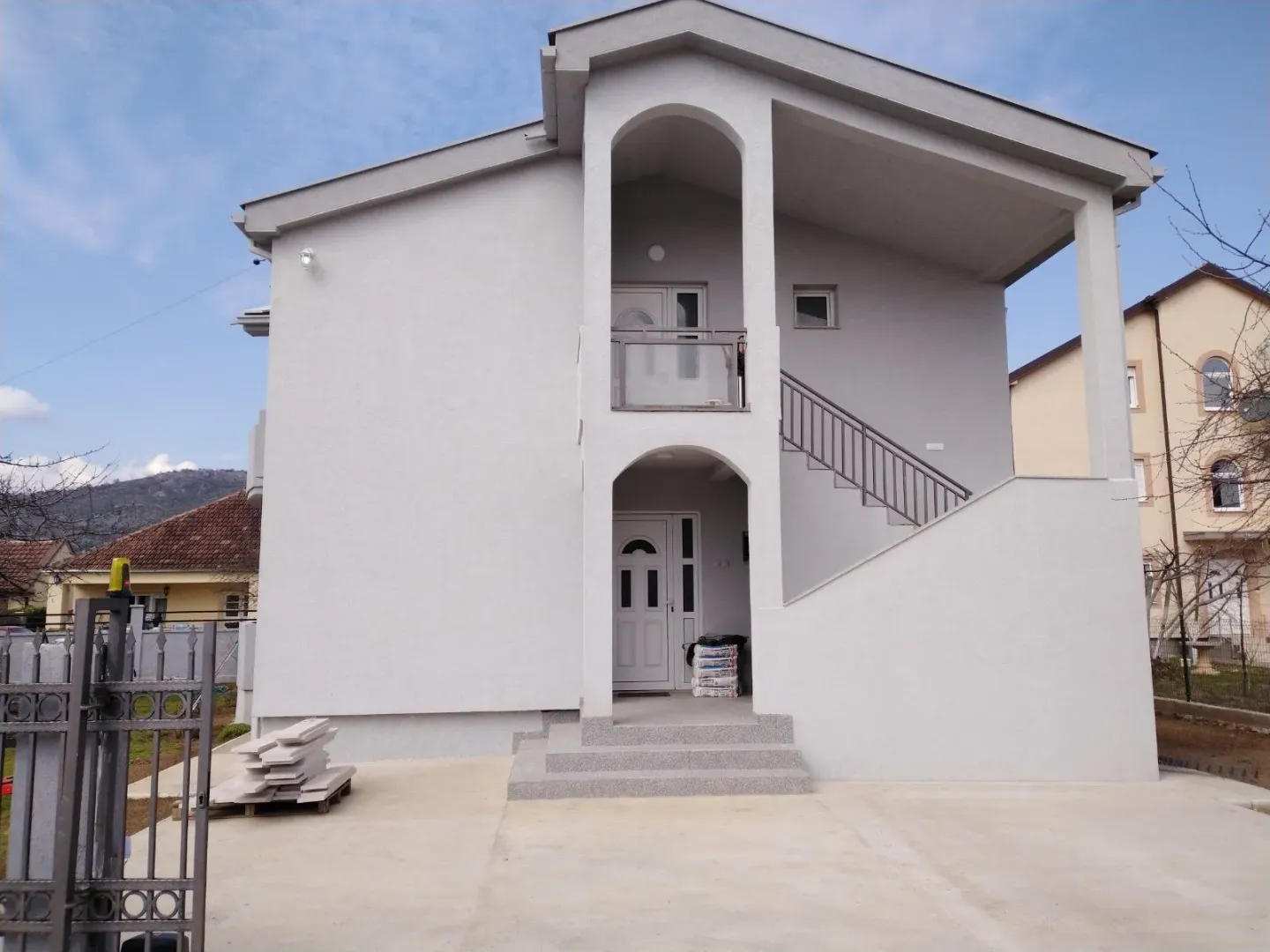 Exterior view of a two-story house with a light facade and outdoor stairs.