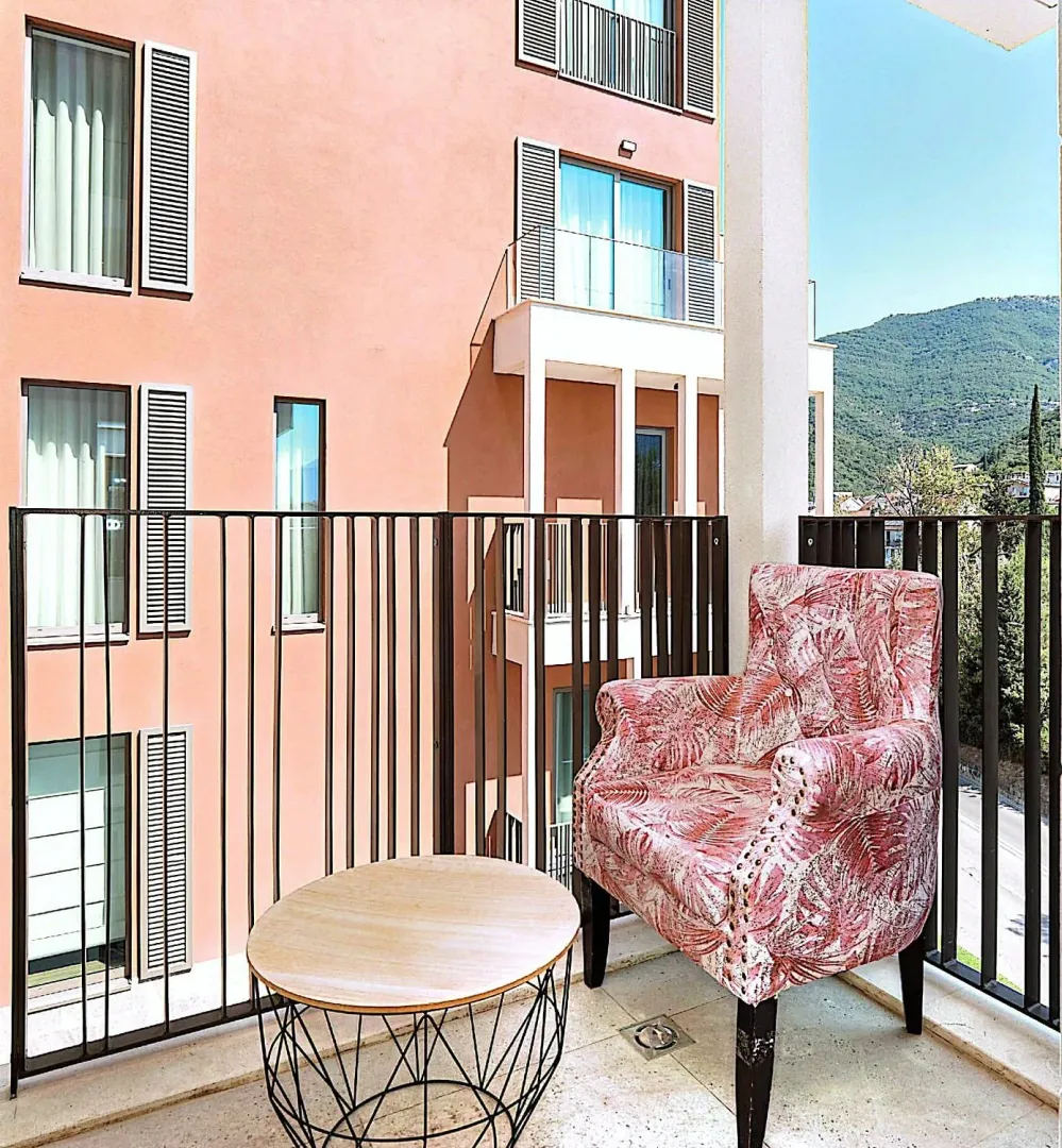 Natkriveni balkon sa foteljom, stočićem i pogledom na zgradu i brda.