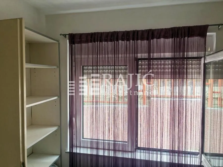 View of a window with dark curtains and shelves on the left side.