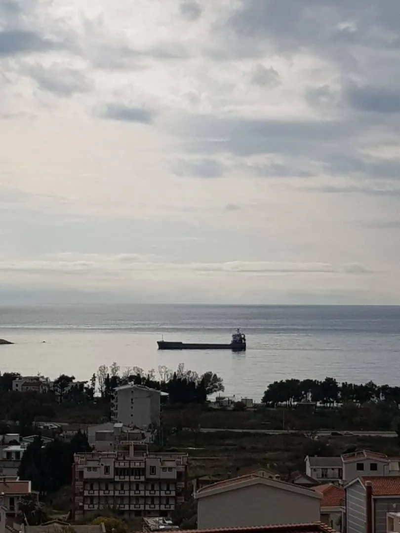 Pogled s visine na more, brod u daljini i okolna naselja pod oblačnim nebom.