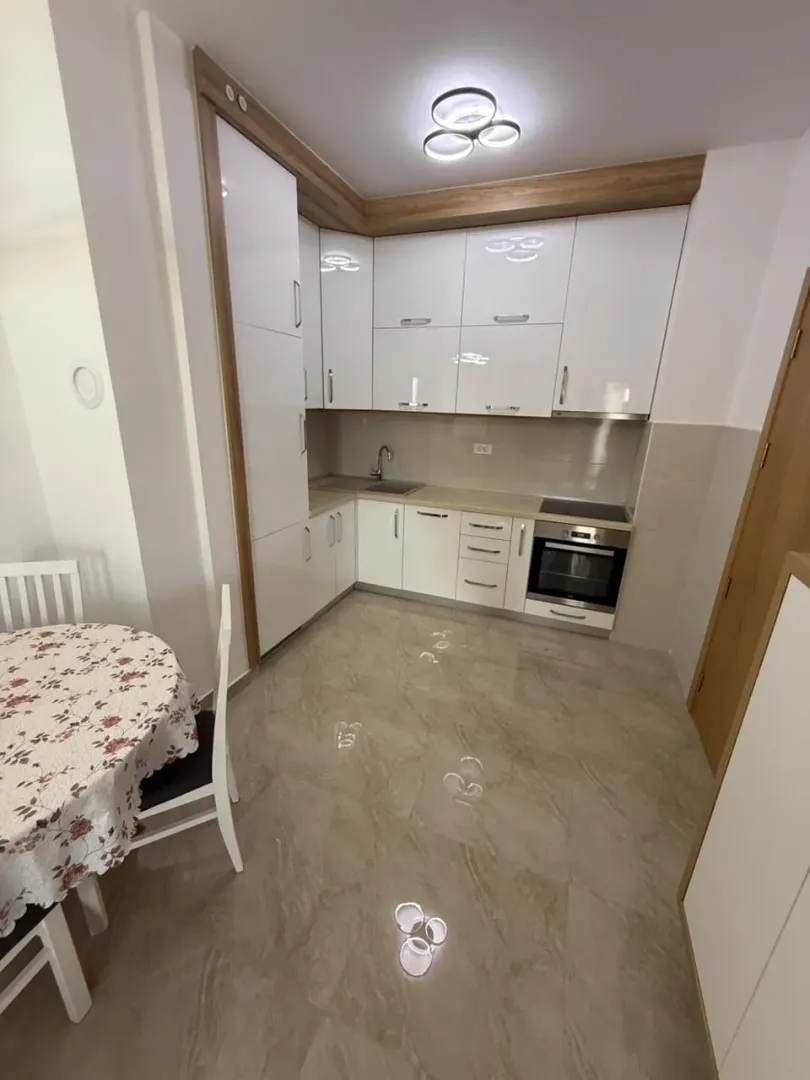 Moderna bijela kuhinja sa ugradnim elementima i trpezarijskim stolom.