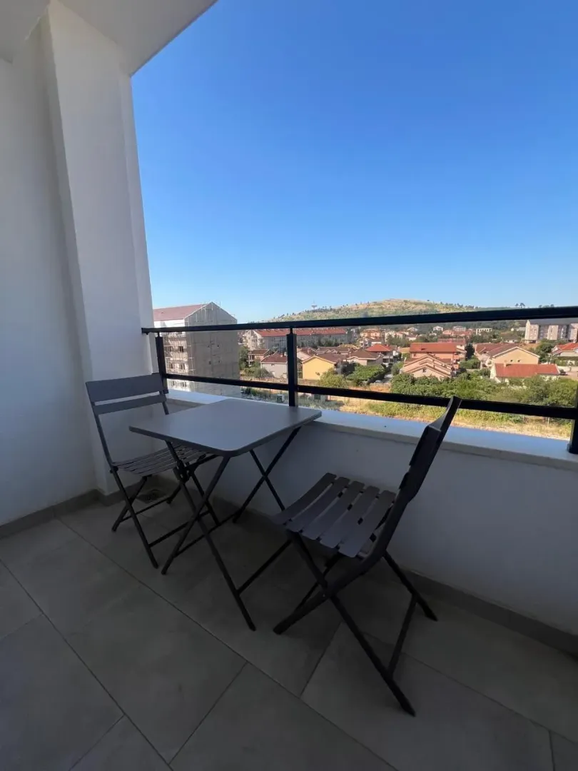 Natkriveni balkon sa malim stolom, dvije stolice i pogledom na naselje.