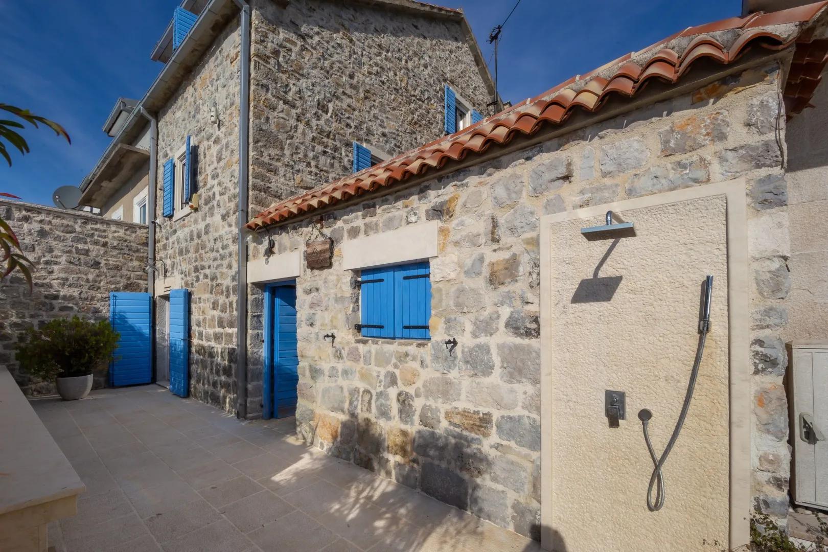 Exterior of a stone house with blue shutters and a paved courtyard.