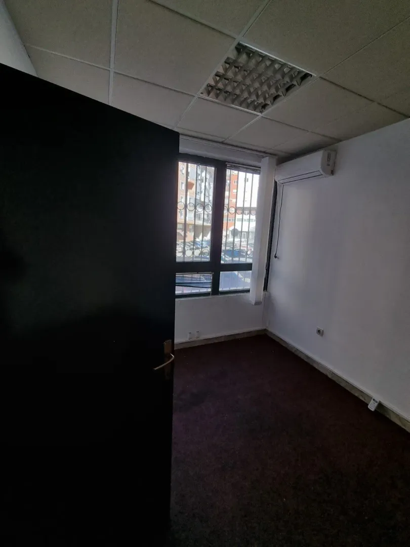 An empty room with a window, dark carpet, and an air conditioner.