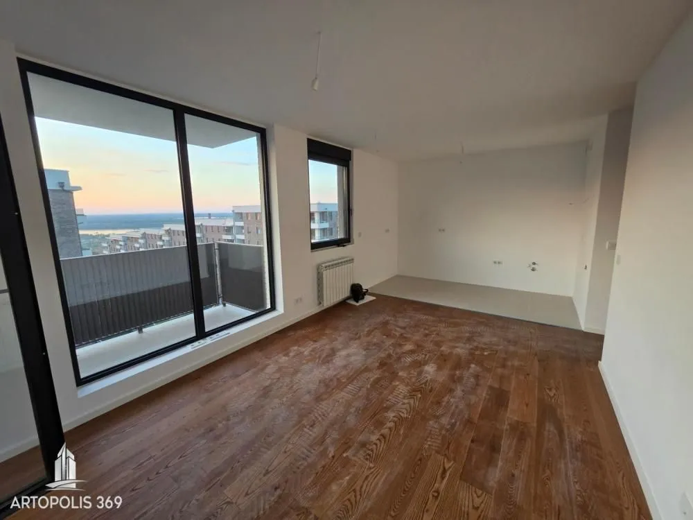 View of an unfurnished room with wooden flooring and a large window overlooking the city.