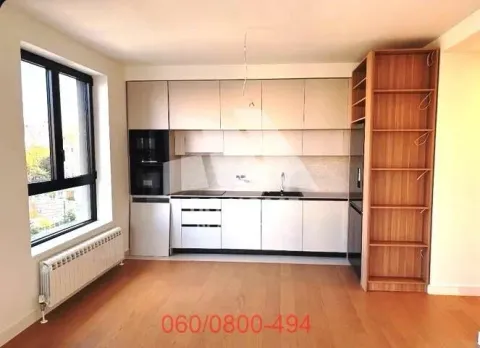 Moderna kuhinja sa belim elementima, drvenim podom i velikim prozorom. - image 2