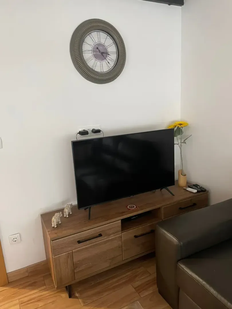 Dnevna soba sa televizorom na drvenoj komodi i zidnim satom.