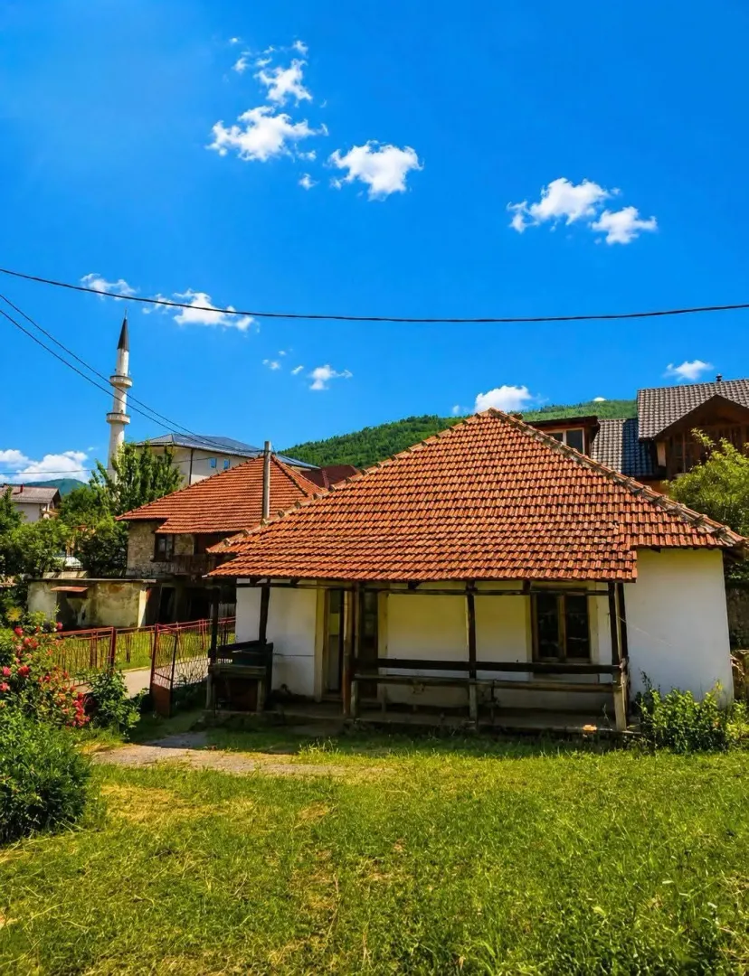 Pogled na stariju prizemnu kuću sa krovom od crijepa i travnatim dvorištem.