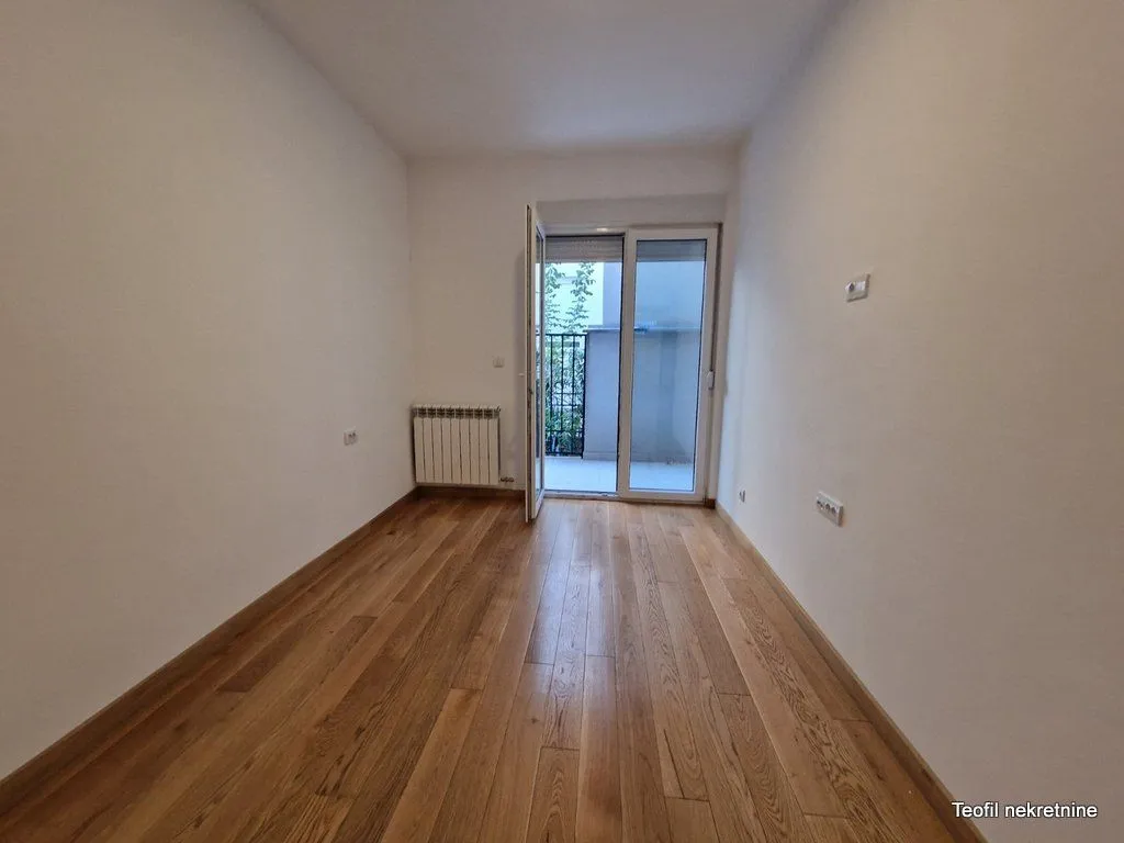 Prazna soba sa drvenim podom i izlazom na terasu.