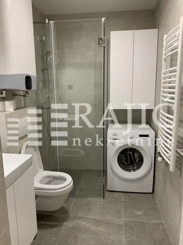 Moderno opremljeno kupatilo sa tuš kabinom i veš mašinom.