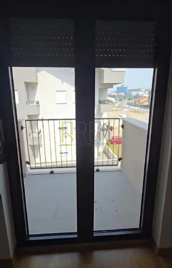 Pogled kroz balkonska vrata na terasu i okolne zgrade.