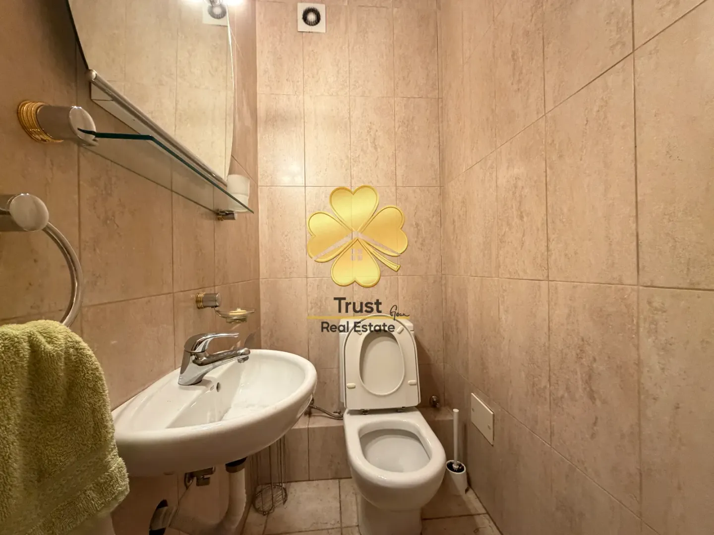 Manje kupatilo sa umivaonikom i šoljom obloženo bež pločicama.