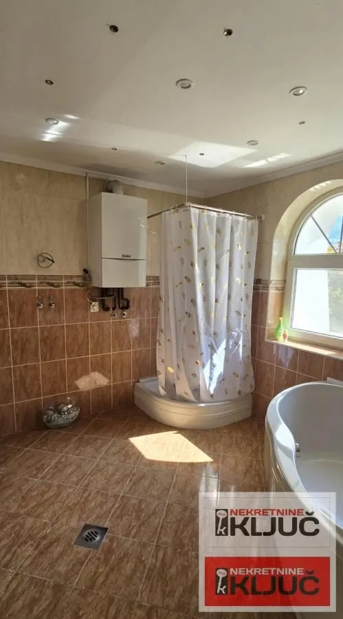 Tiled bathroom with a shower cabin, bathtub, and boiler.