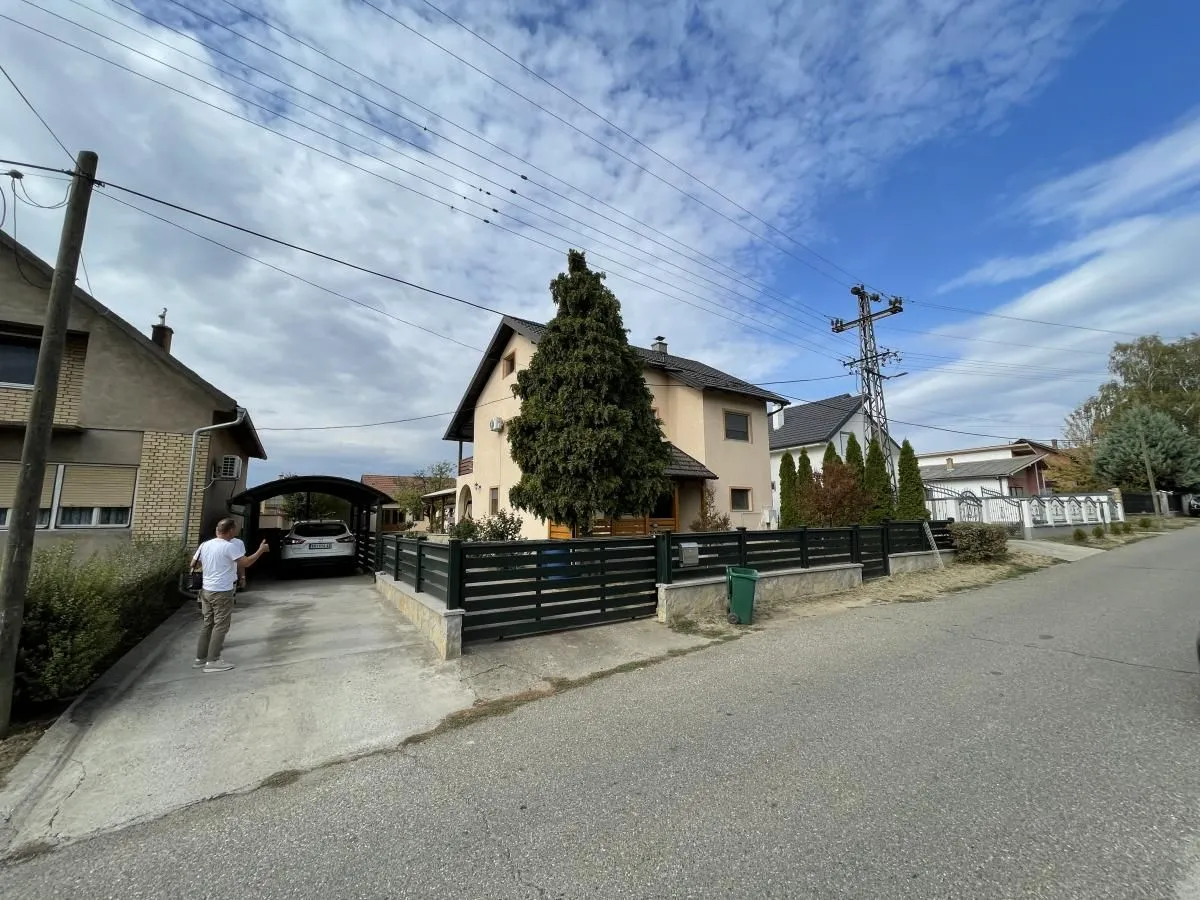 Pogled na spoljašnjost kuće sa dvorištem, ogradom i prilazom sa parkingom.