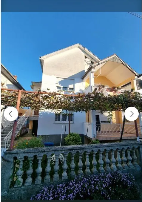 Dvospratna kuća sa uređenim dvorištem i lozom ispred terase.