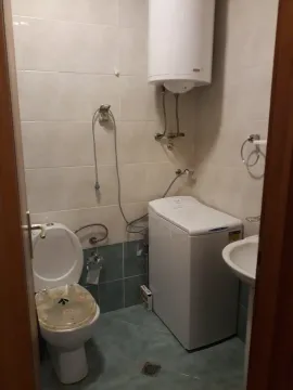 A simple bathroom featuring a toilet, washing machine, and water heater. - image 6