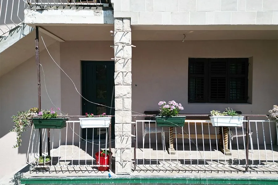 Terrace with metal railing decorated with flower pots in front of the house entrance.