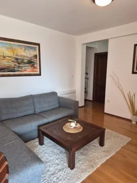 Dnevna soba sa sivom ugaonom garniturom, drvenim stočićem i slikom na zidu. - image 9