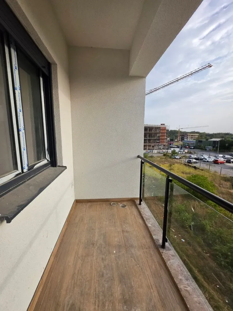 Prazan nenamješten balkon sa pogledom na okolinu i gradilište.