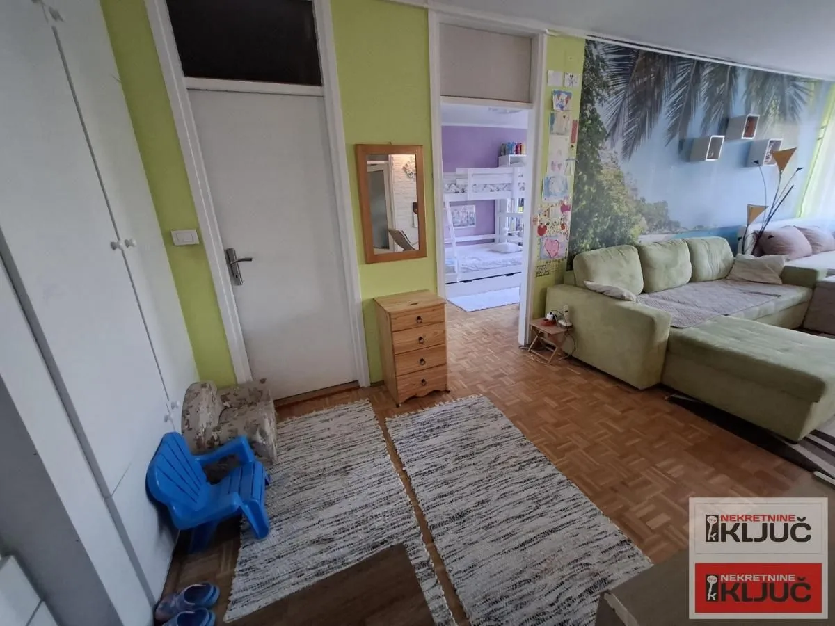 Dnevna soba sa garniturom, parketom i prolazom u drugu prostoriju.