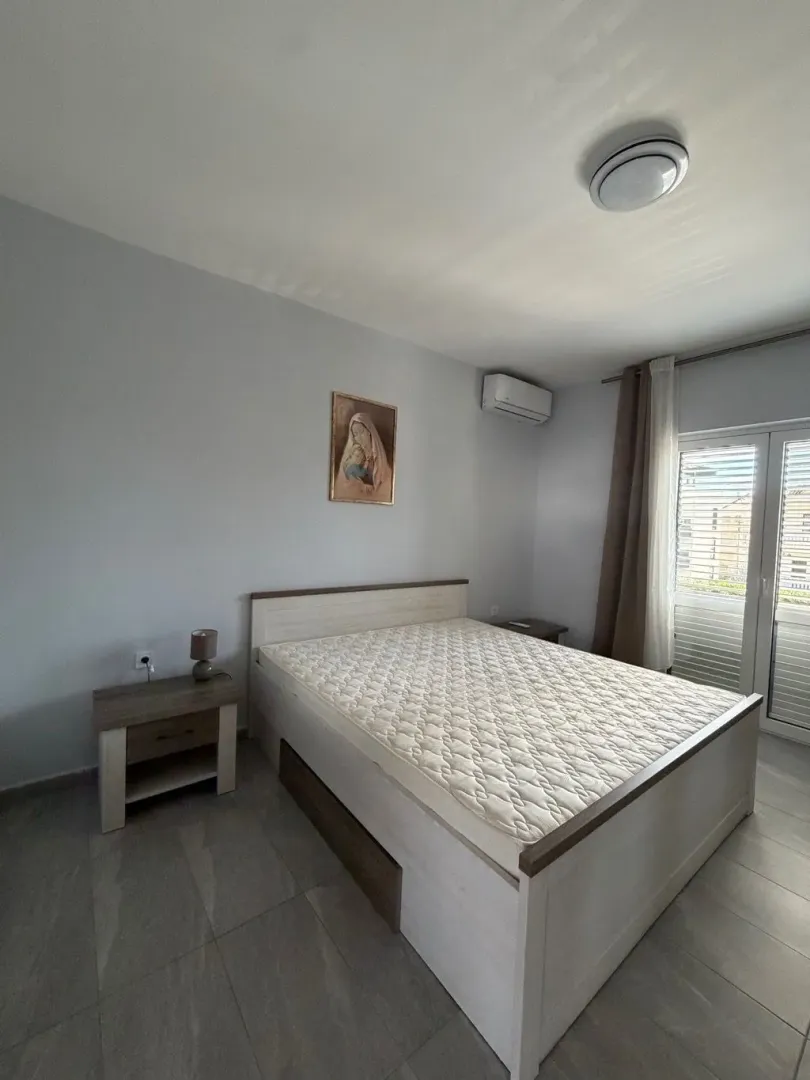 Svijetla spavaća soba sa bračnim krevetom i noćnim stočićima.