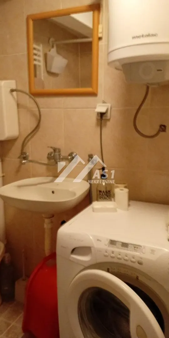 Manje kupatilo sa umivaonikom, ogledalom i veš mašinom.