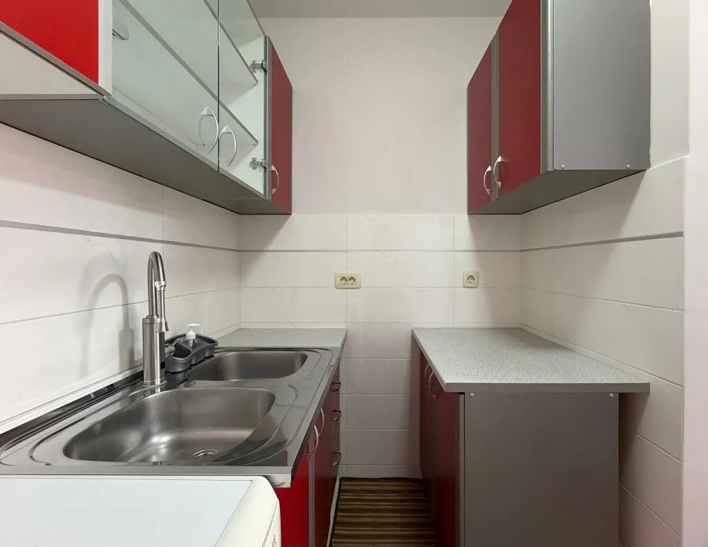Small kitchen with a sink, countertops, and red and grey wall cabinets.