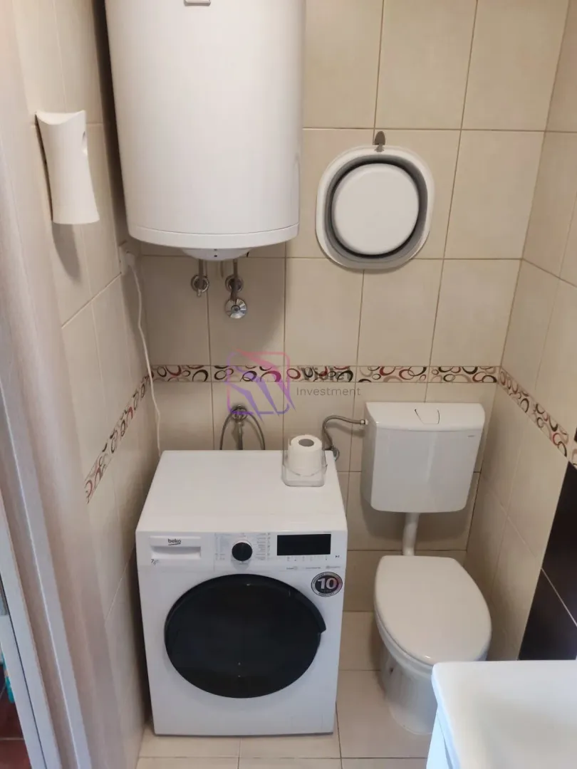 Manje kupatilo sa WC šoljom, veš mašinom i bojlerom na zidu.