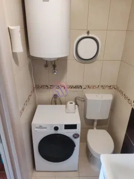 Manje kupatilo sa WC šoljom, veš mašinom i bojlerom na zidu. - image 9