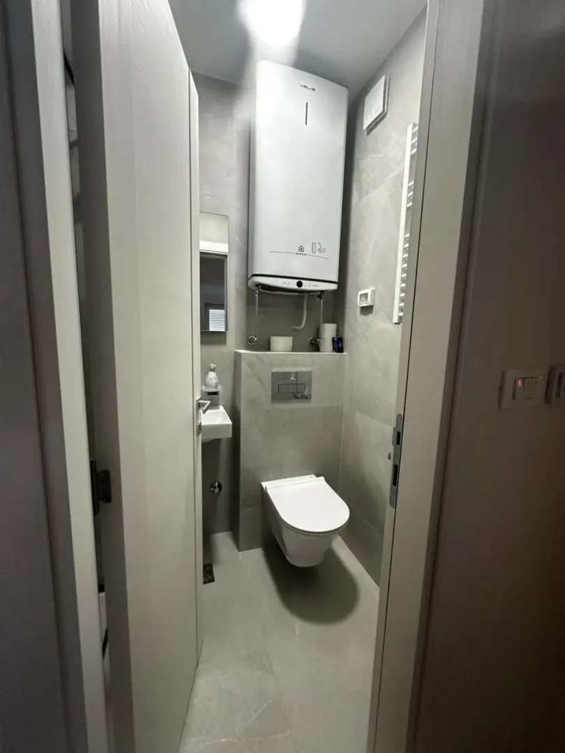 Smaller bathroom with a toilet, sink, and water heater on the wall.