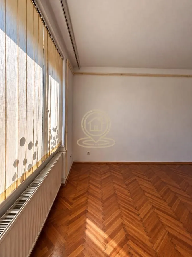 Empty room with hardwood floors and a window with blinds.