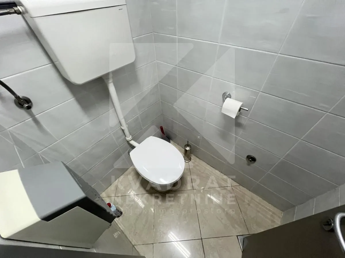 Small bathroom tiled with light tiles, featuring a toilet and a concealed cistern.