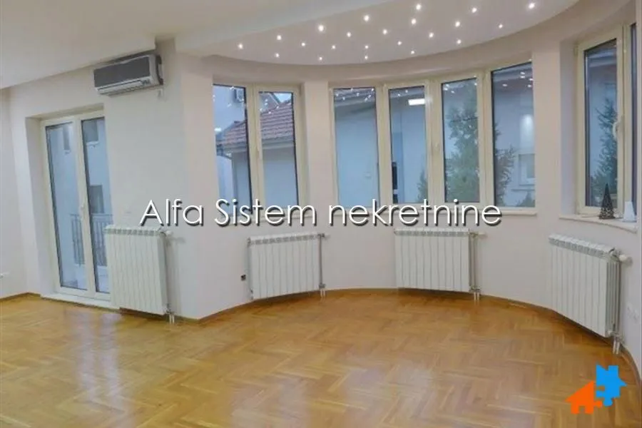 Empty living room with parquet flooring, radiators, and large windows set in a semicircular wall.