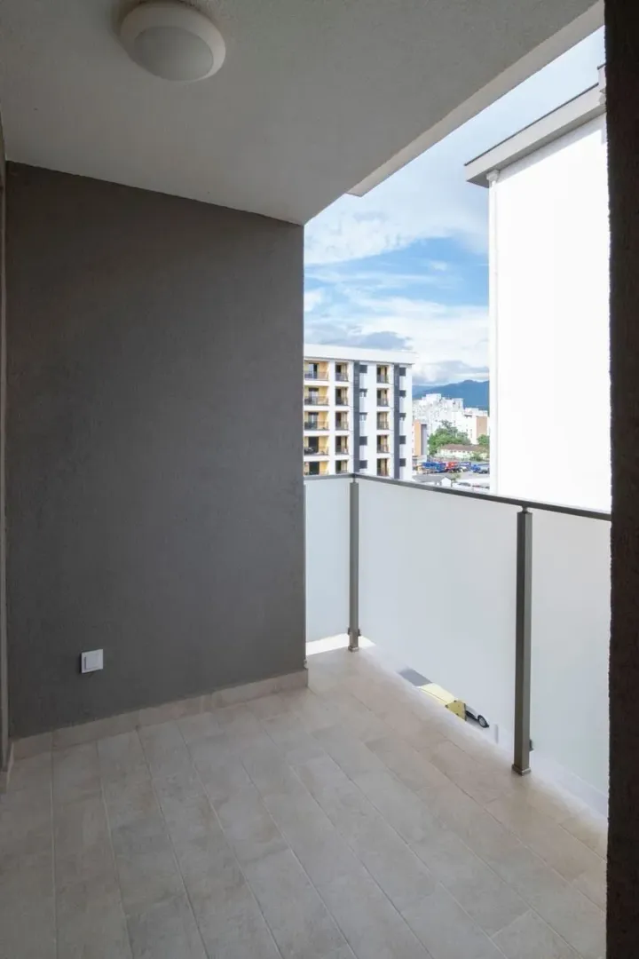 An empty balcony with a glass railing and a view of surrounding buildings.