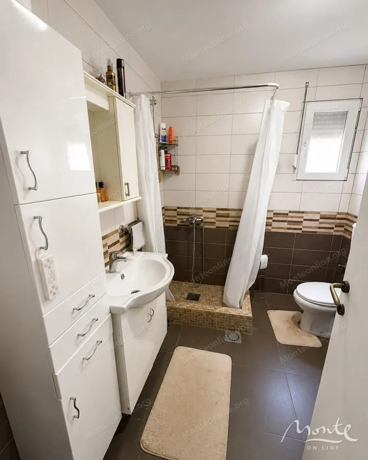 Kupatilo opremljeno umivaonikom, tuš kabinom, WC šoljom i bijelim ormarićem.
