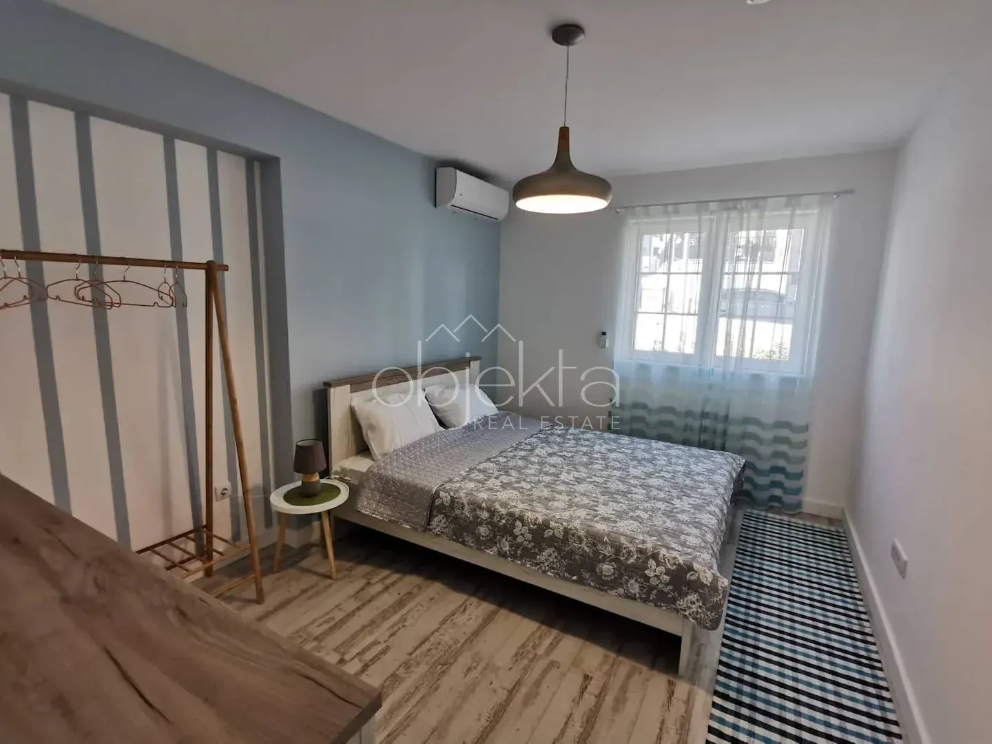 Furnished bedroom with a double bed, wooden clothes rack, and a window.