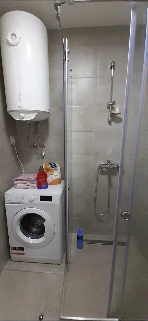 A bathroom featuring a shower cabin, washing machine, and water heater.