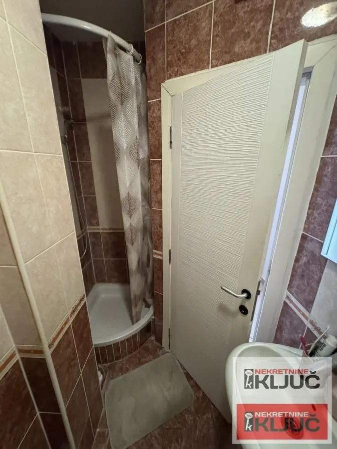 Manje kupatilo sa tuš kabinom obloženom keramičkim pločicama.