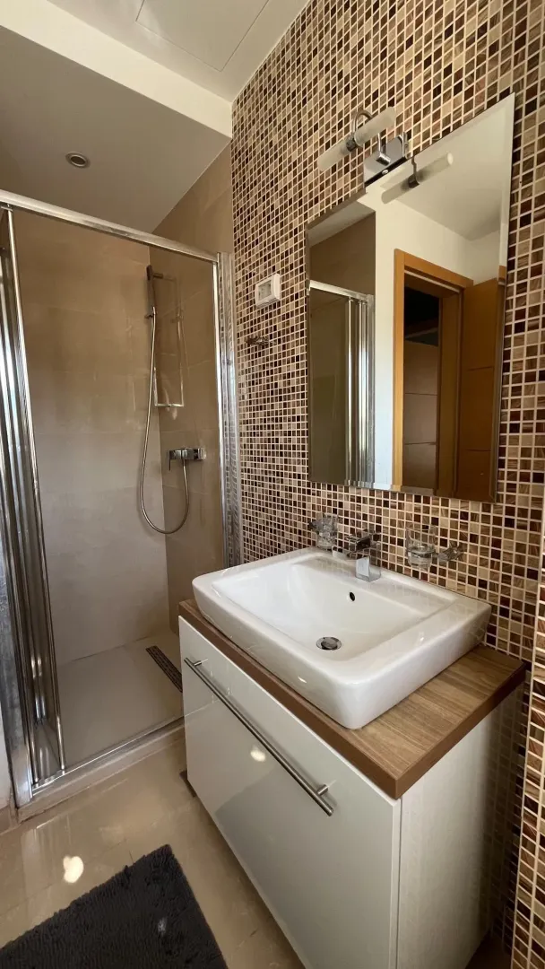 Bathroom with a walk-in shower, vanity sink, and mosaic tiles.