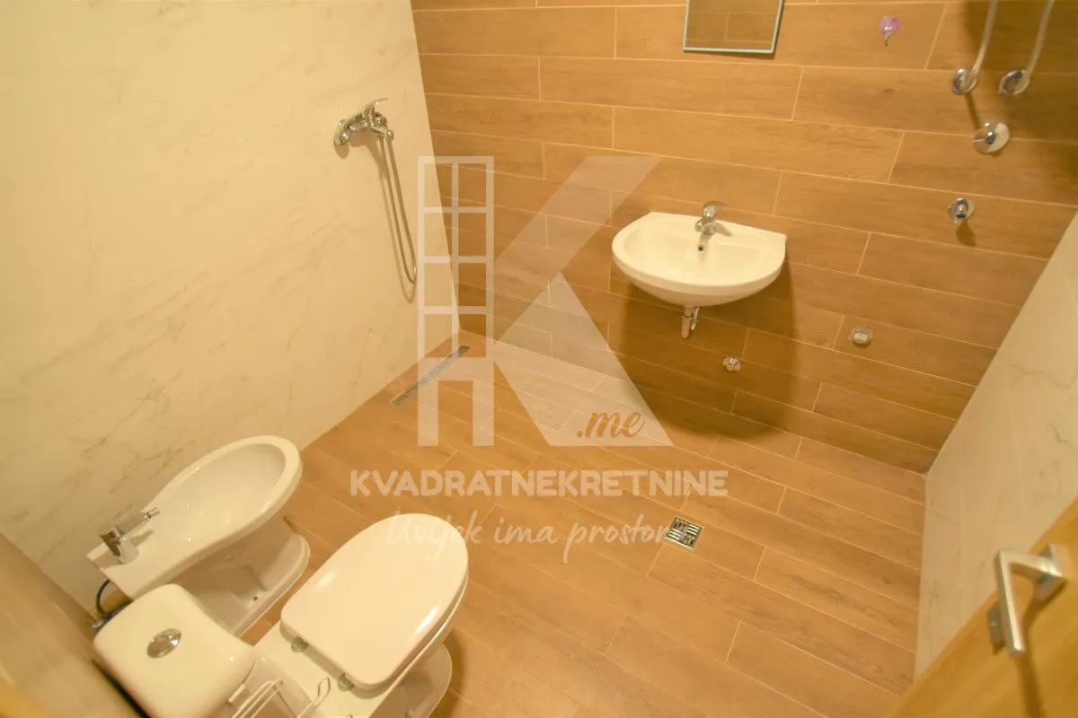 Bathroom equipped with a sink, toilet, bidet, and a shower area with wood-look tiles.