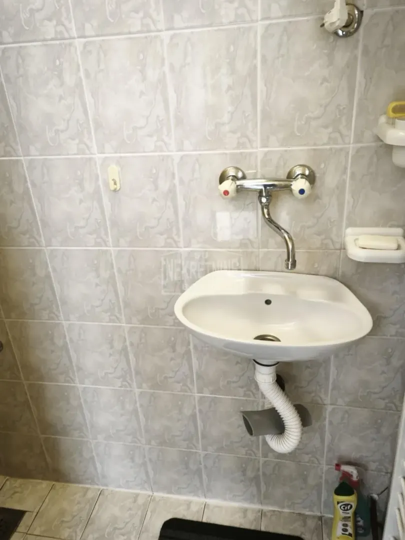 Manji umivaonik sa slavinom montiran na popločani zid kupatila.