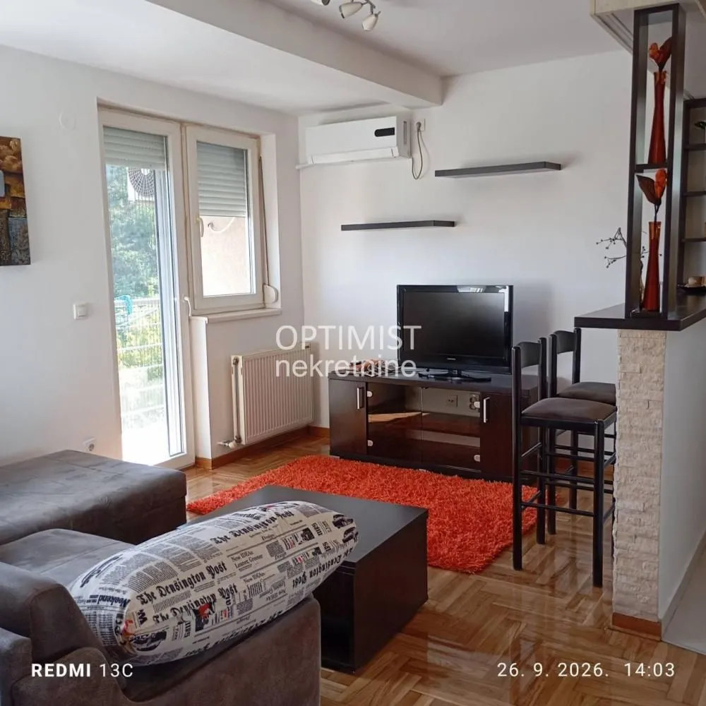 Dnevna soba sa garniturom, televizorom i trpezarijskim delom sa šankom.