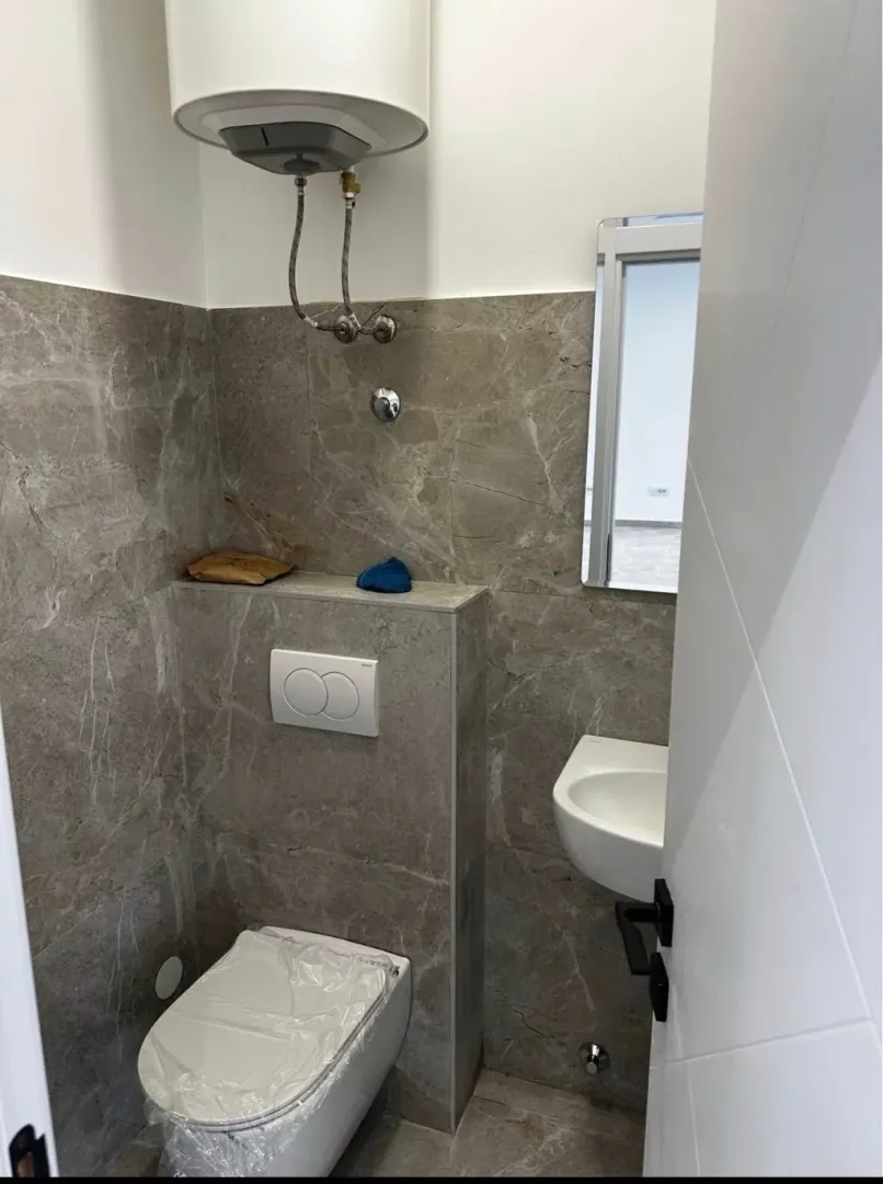 Smaller bathroom tiled with ceramic tiles featuring a built-in toilet and water heater.
