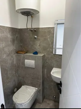 Smaller bathroom tiled with ceramic tiles featuring a built-in toilet and water heater. - image 6