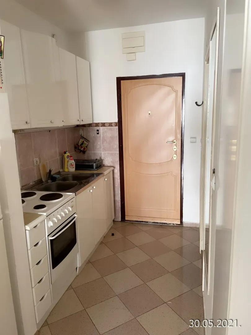 Small white kitchen with a stove and sink next to the entrance door.