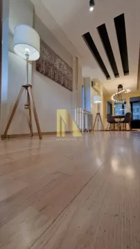 Prostrani dnevni boravak sa drvenim podom, modernim osvetljenjem i trpezarijom u pozadini. - image 7
