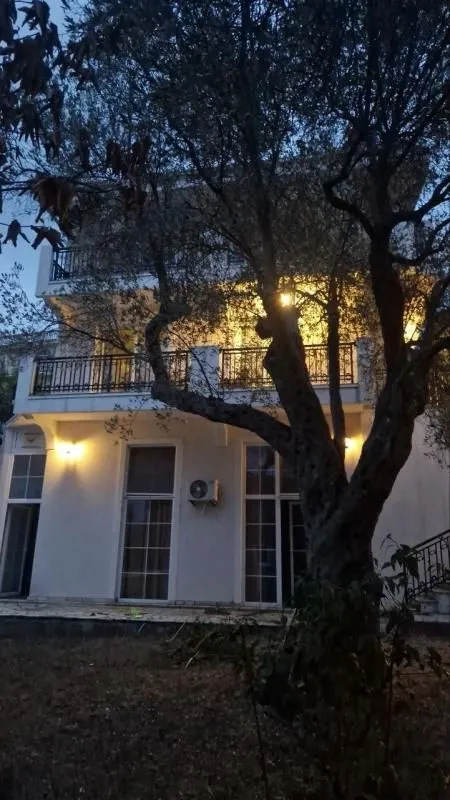 View of the exterior of the house with a balcony and a tree in the yard at dusk.
