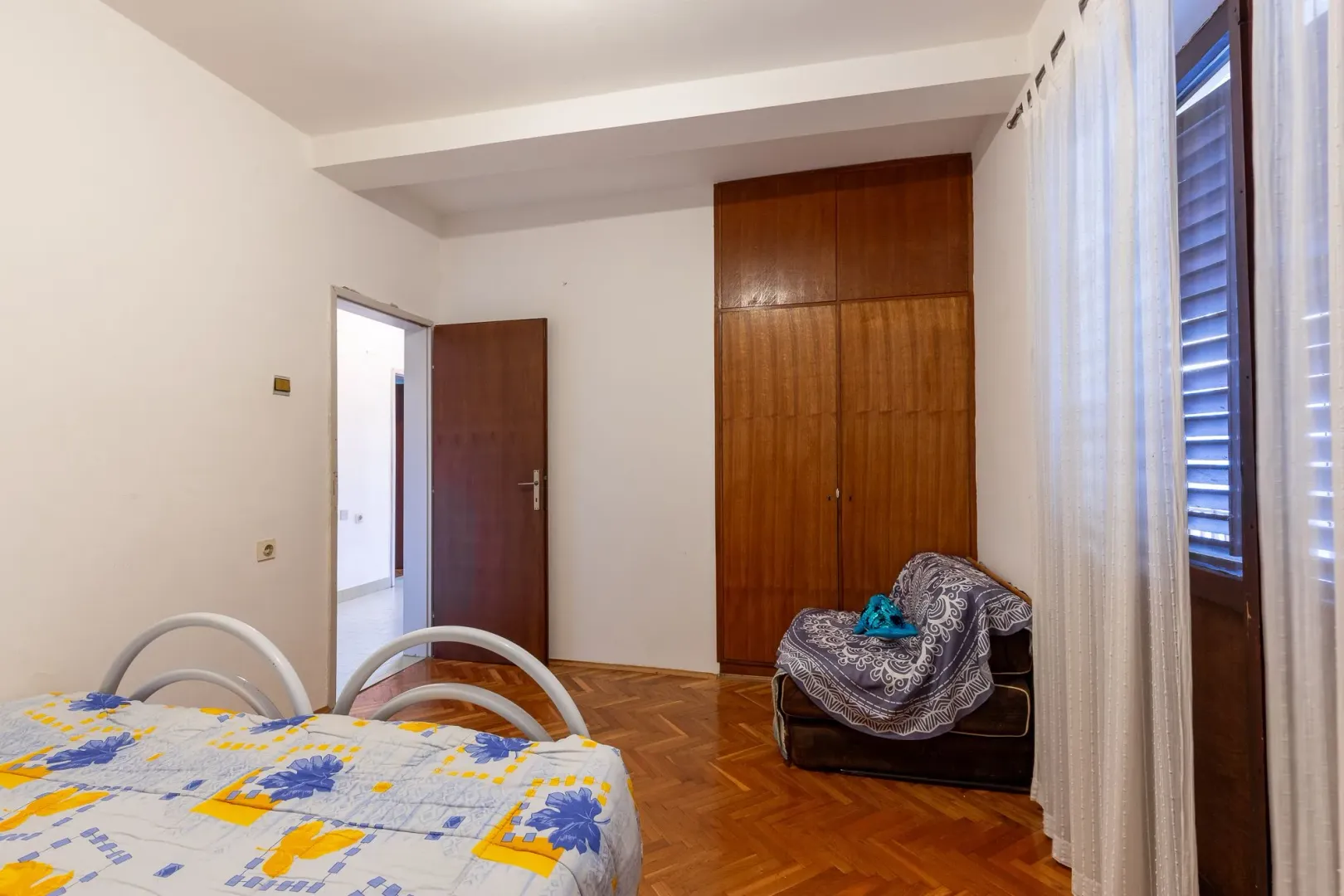 Spavaća soba sa krevetom, drvenim ormanom i prozorom sa zavesama.