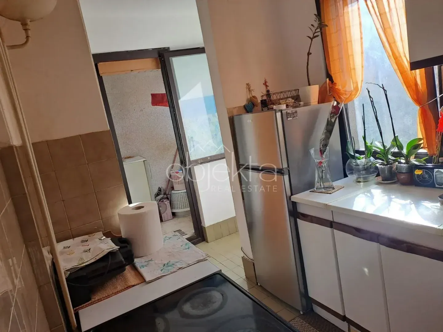 Pogled na manju kuhinju sa bijelim elementima, frižiderom i šporetom.